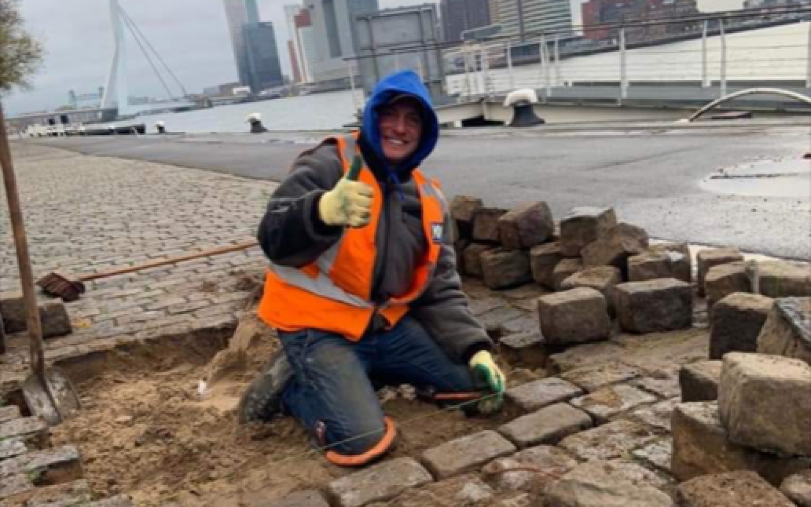 Stratenmaker van KVDM Groep legt keien op een kade met de Erasmusbrug op de achtergrond